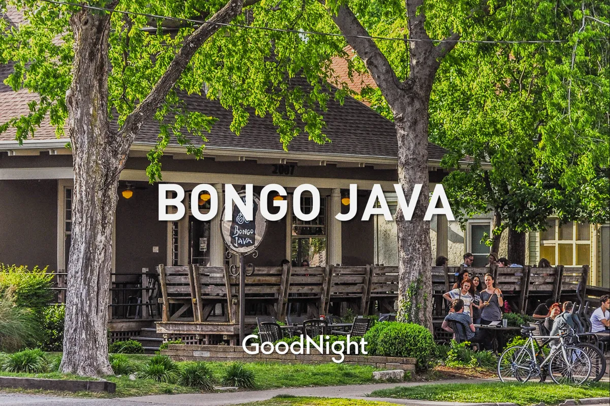 An exterior shot of 'Bongo Java' café, featuring a relaxed outdoor seating area shaded by large trees. People are seen socializing, sipping drinks, and enjoying the fresh air, which highlights the area's dog-friendly patio culture and communal vibe.