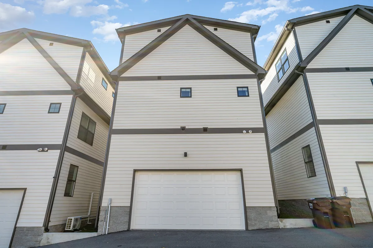 A view of the home's exterior featuring the garage door and clean architectural lines, with the driveway visible and hints of neighboring homes, suggesting a welcoming and secure environment.
