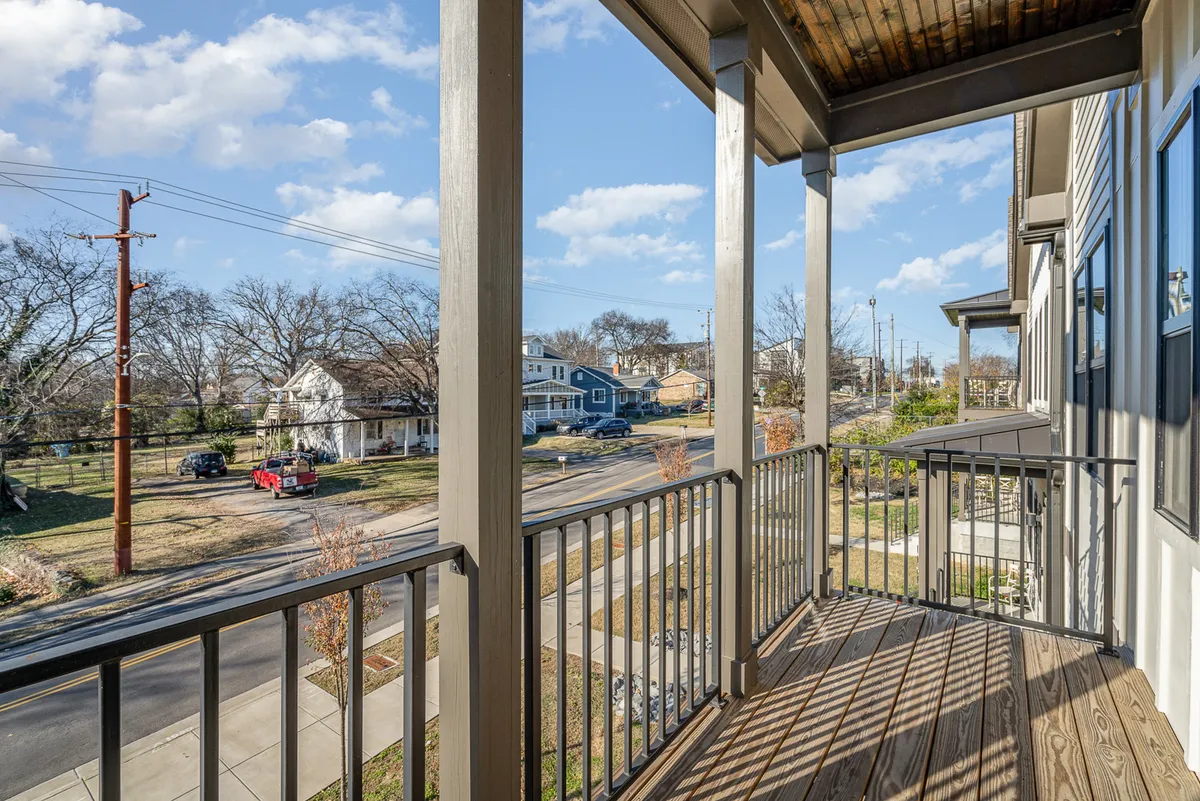 This image captures a second-story balcony with wooden flooring and distinctive railings, surrounded by tranquil neighborhood views and a clear sky. The setting suggests a peaceful retreat, ideal for enjoying coffee in the morning, reading, or simply watching the world go by.