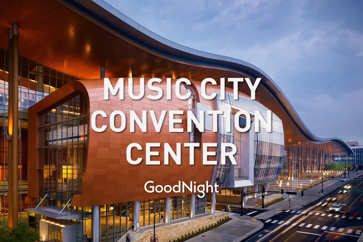 This image showcases the distinctive exterior architecture of a modern building illuminated by warm lighting, with expansive glass windows reflecting the urban surroundings. The vibrant façade signals a welcoming space for conventions, exhibitions, and community gatherings.